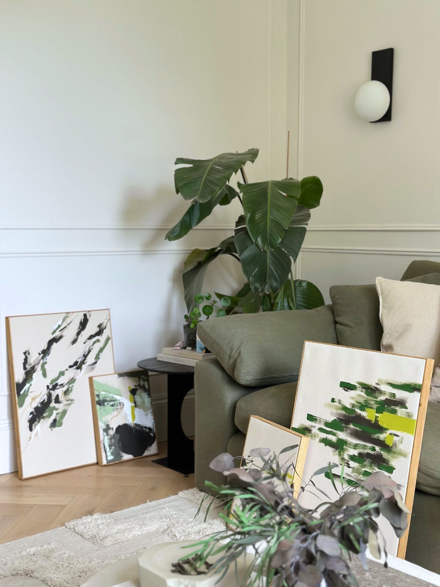Wide living room scene featuring four olive abstract artworks created using the framed canvas double art kit, styled with plants, textiles and neutral decor.
