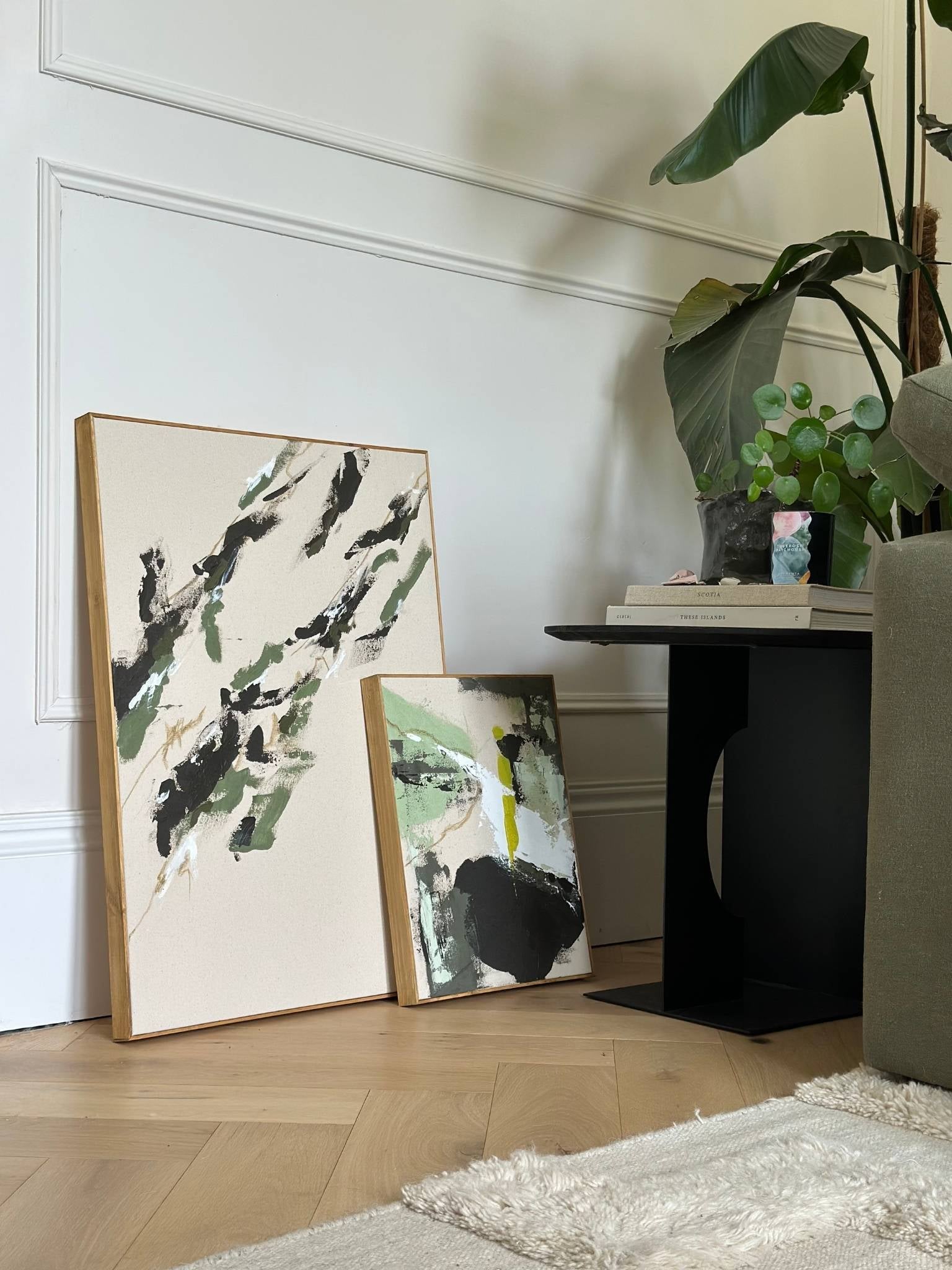 Styled interior view of two olive-toned abstract artworks created from one framed canvas double art kit, placed beside a sofa and indoor plants.