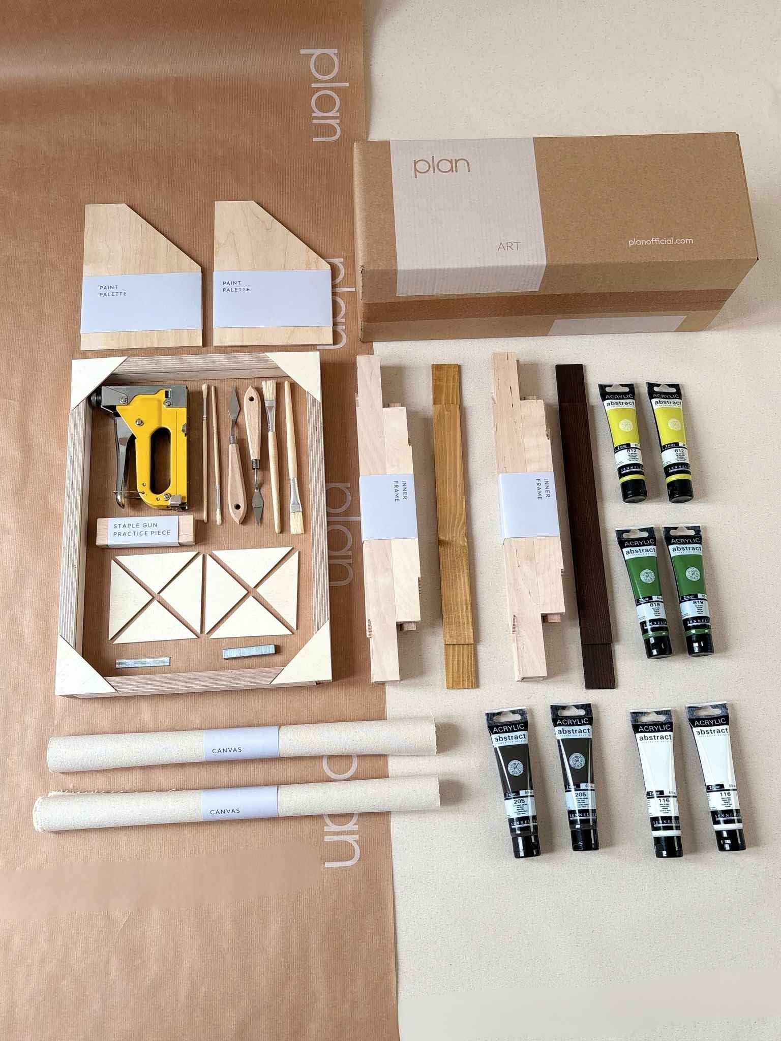 Two finished abstract artworks created using the Olive framed canvas double art kit, leaning against a wall beneath a window in a calm, neutral living space.