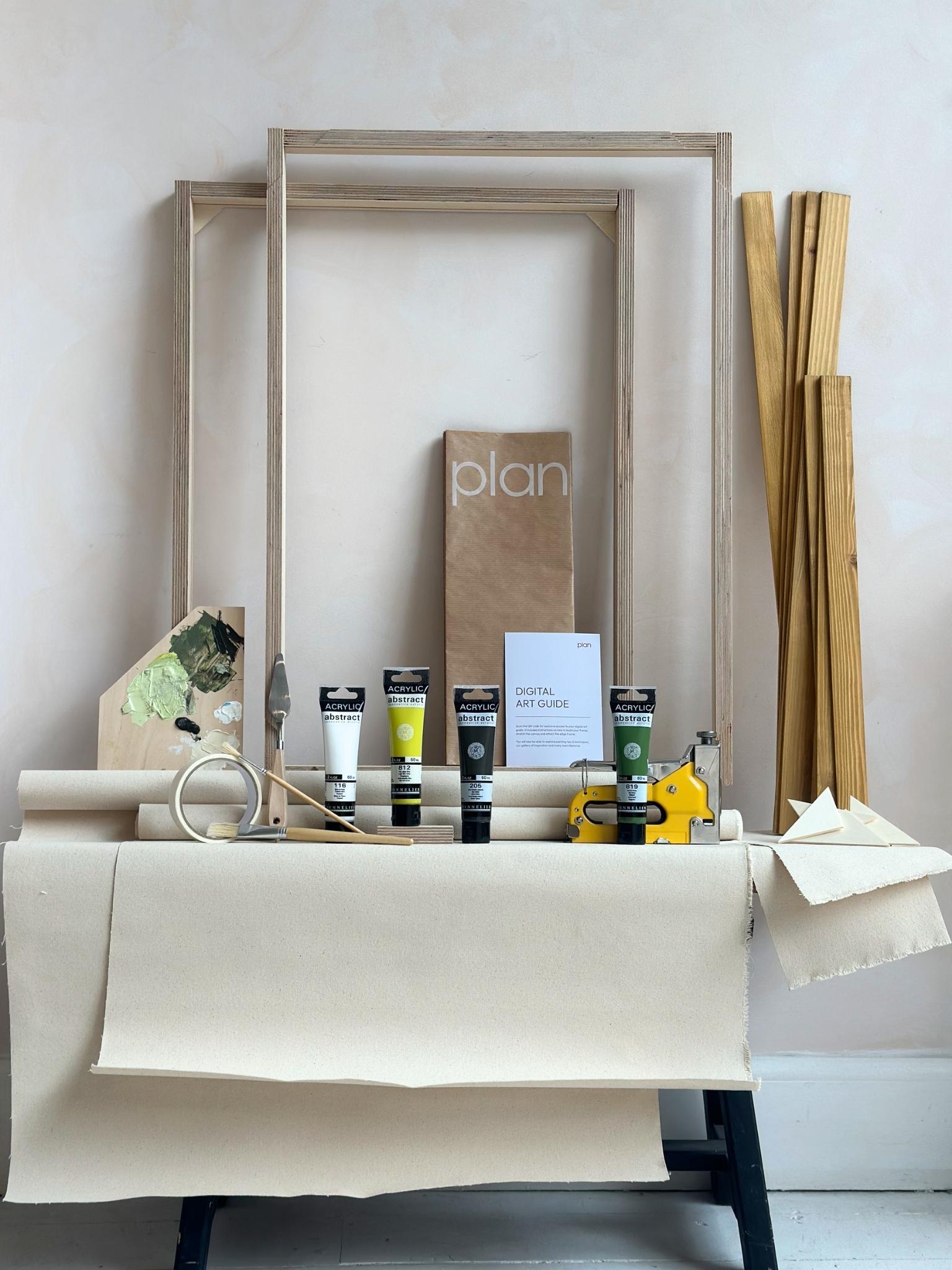 Two finished abstract artworks created using the Olive framed canvas double art kit, leaning against a wall beneath a window in a calm, neutral living space.