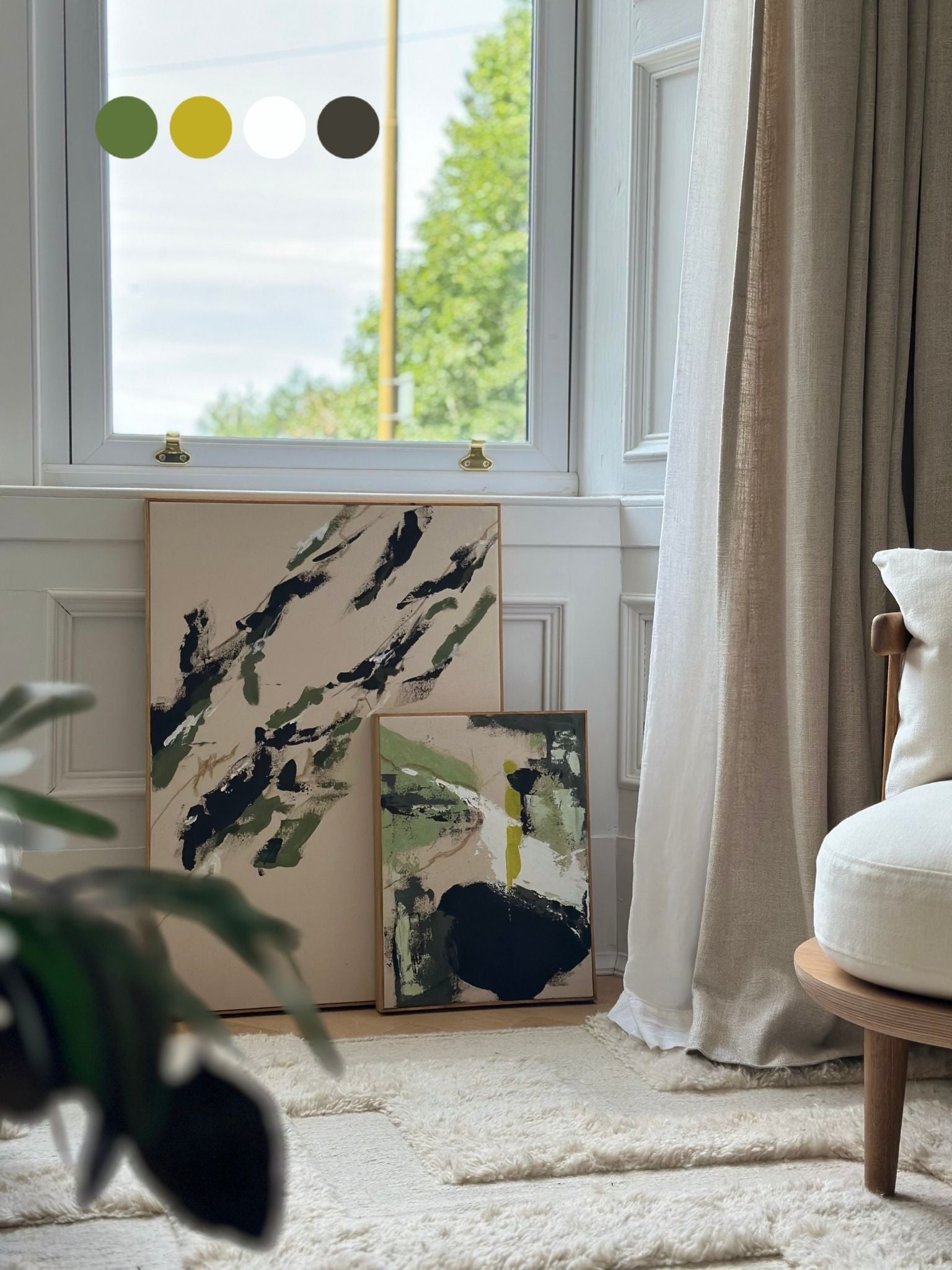 Two finished abstract artworks created using the Olive framed canvas double art kit, leaning against a wall beneath a window in a calm, neutral living space.