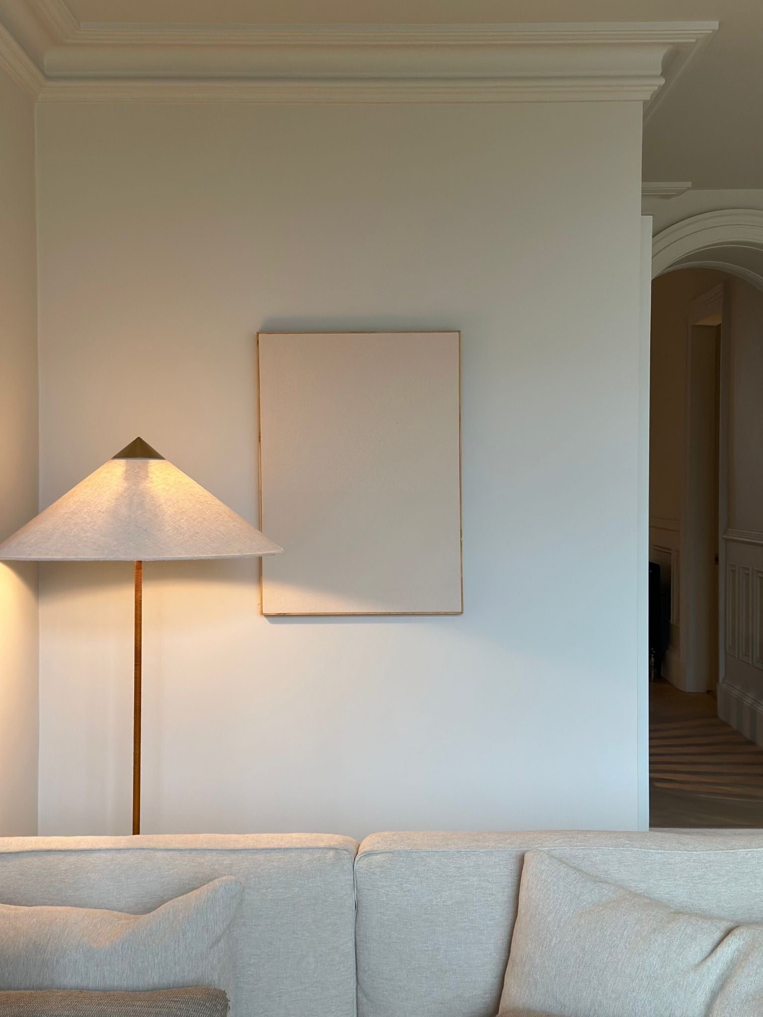 Single blank framed cotton canvas from a DIY art kit styled above a sofa with floor lamp in a calm, neutral living room.