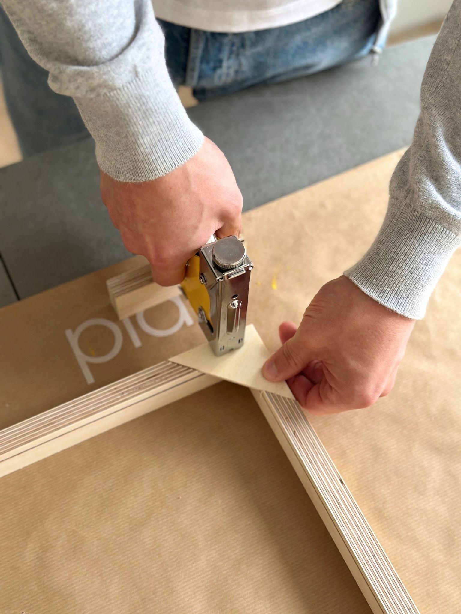 Hands stapling handcrafted, custom wooden inner frame using a staple gun as part of a DIY framed linen canvas art kit