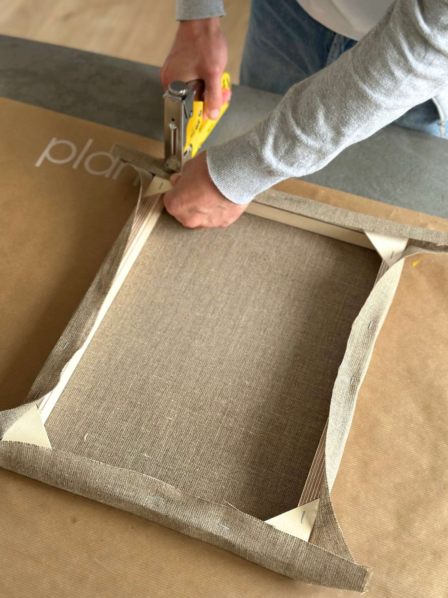 Back view of a linen canvas neatly stretched and stapled onto a wooden inner frame during the canvas stretching process of a DIY art kit