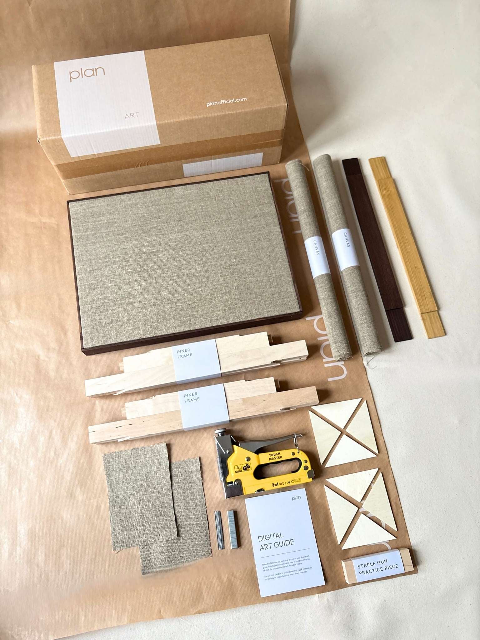 Two blank DIY framed linen canvases leaning on a wooden bench behind a neutral sofa with rust cushions, styled in a minimalist living room.