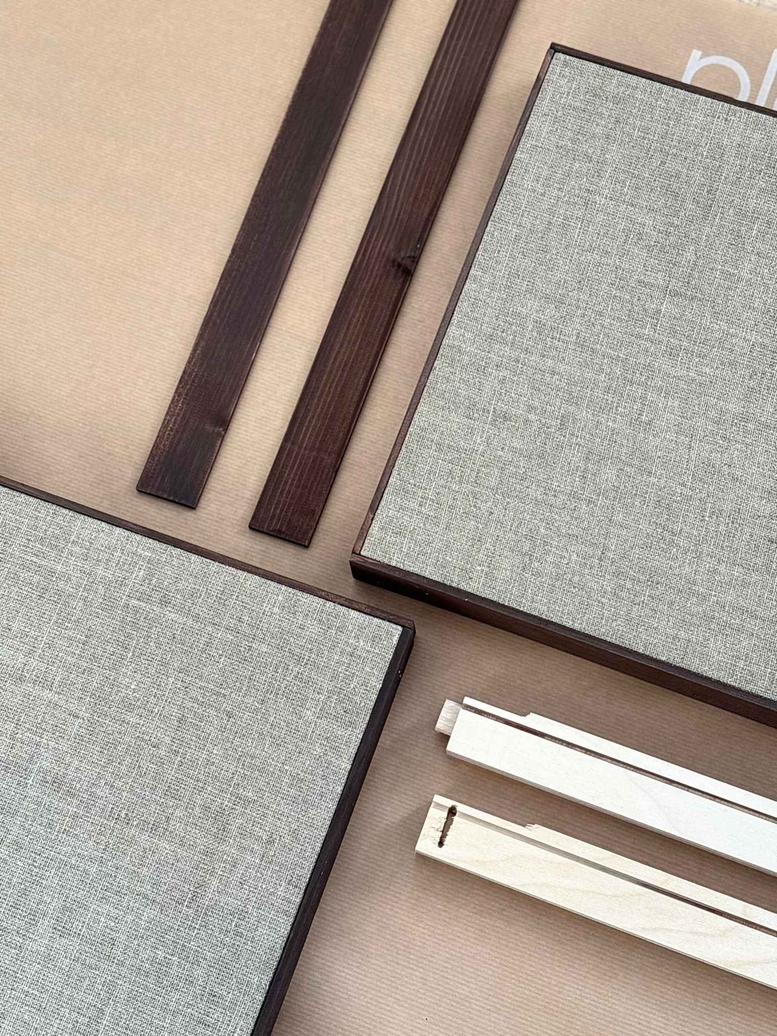 Close-up flat lay of dark oak edge frame pieces and stretched linen canvases, part of a DIY framed linen canvas art kit designed to create gallery-style artwork at home.