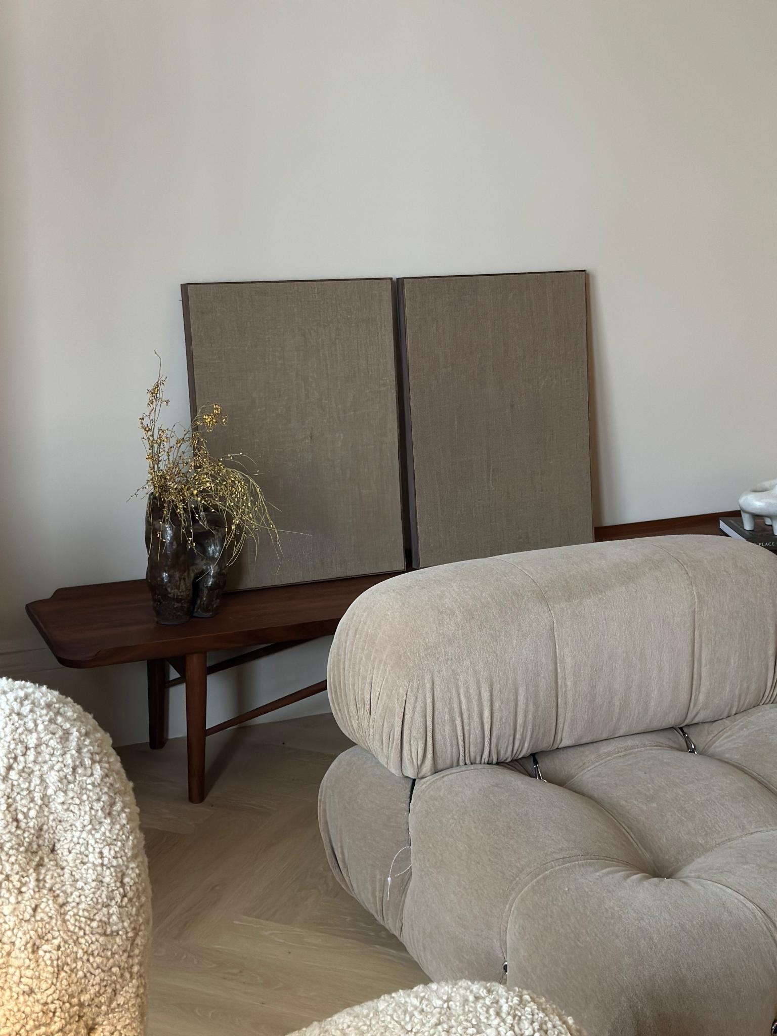 Two blank framed linen canvases from Plan Art Kits leaning side by side on a wooden console table behind a sofa, styled with a dark vase and dried stems.