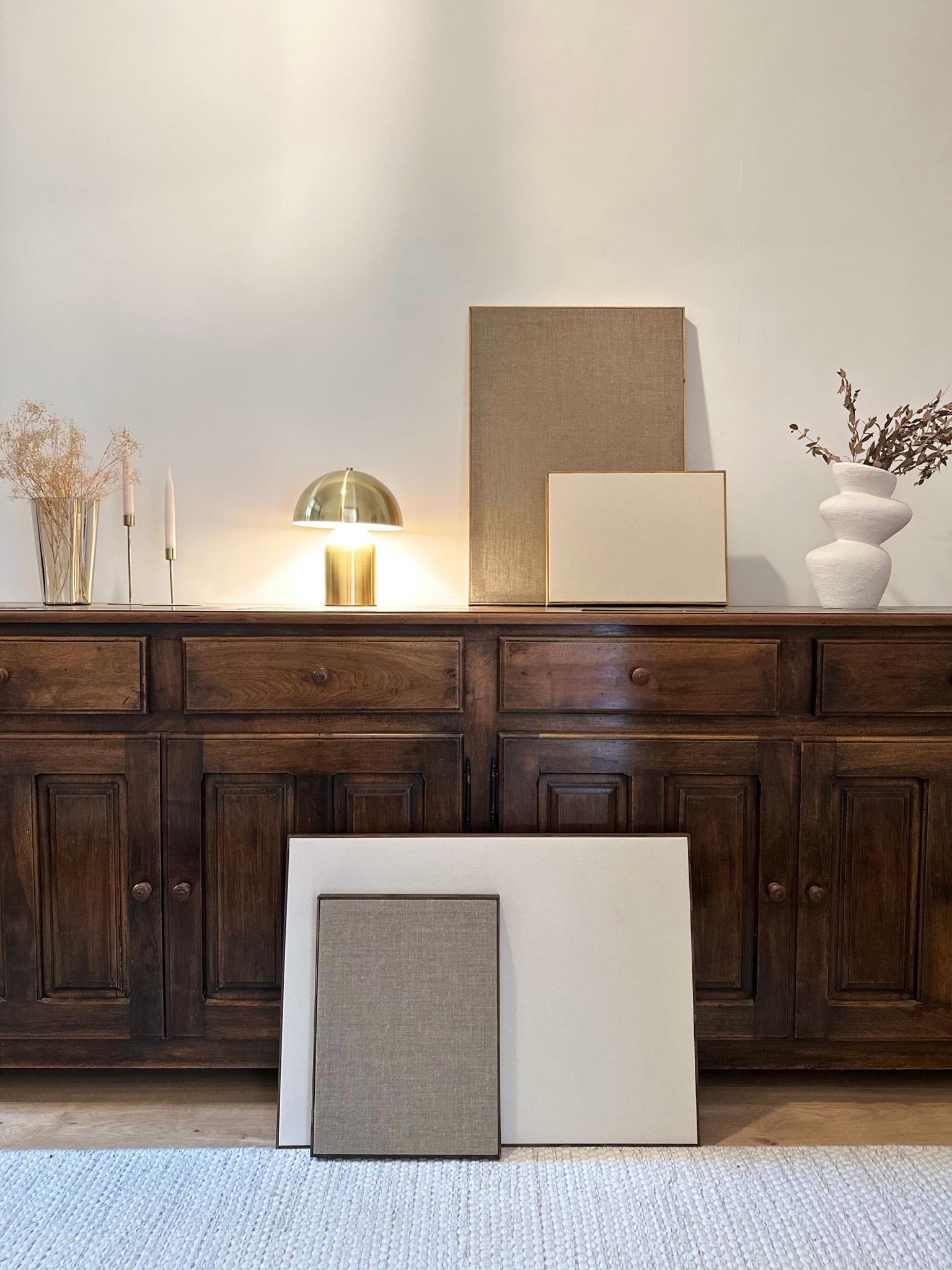 Styled framed blank canvas artworks leaning against a dark wooden sideboard, showing neutral cotton and linen canvases in oak and dark oak edge frames in a minimalist interior setting.