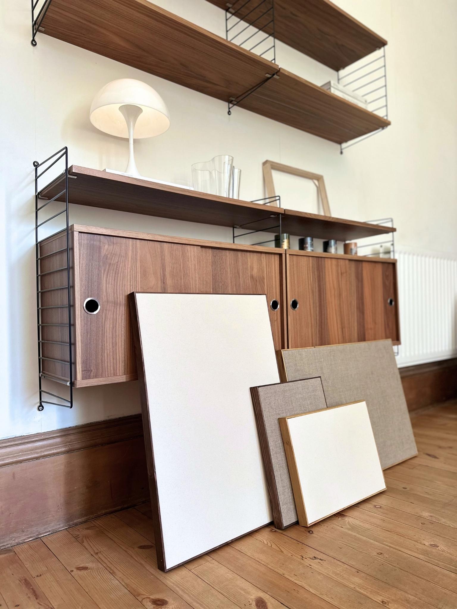 Multiple blank framed canvases in different sizes displayed on wooden shelving, showing cotton and linen canvas textures with oak and dark oak edge frames.