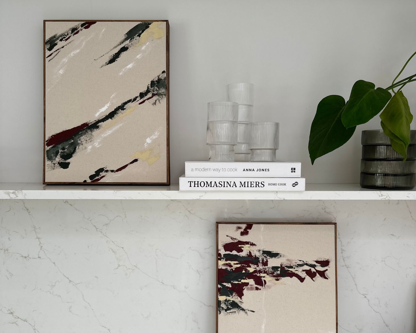 Two framed abstract artworks created with Plan Double Art Kits in Linear aesthetic, displayed on marble shelves beside books and glassware. DIY wall art kits for adults with handcrafted wooden frames.