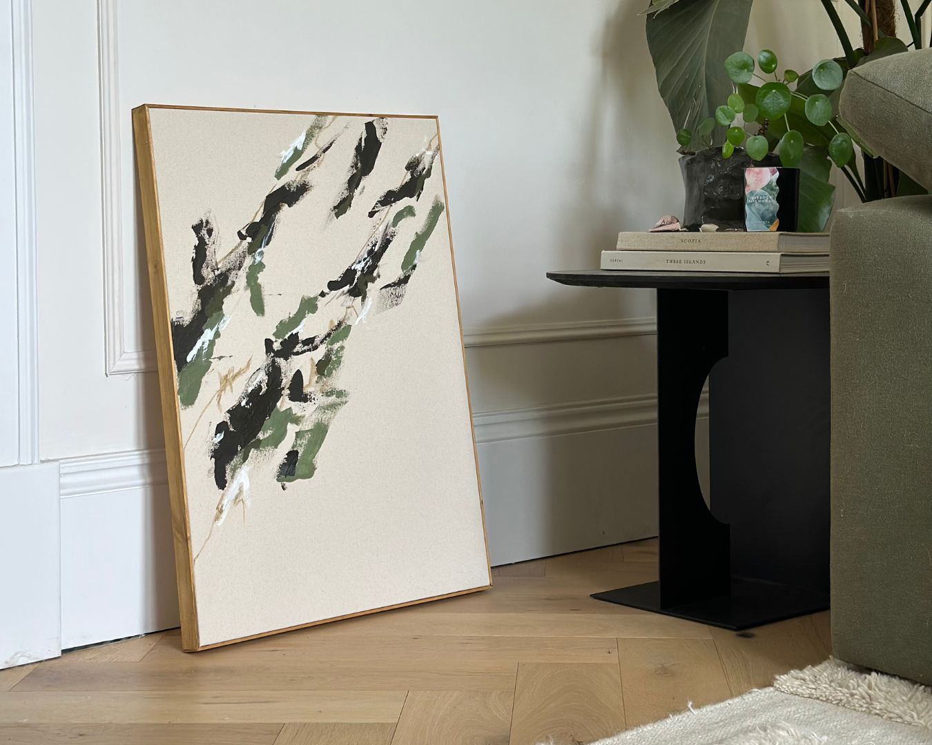 Framed abstract artwork created with a Plan Single Art Kit Linear aesthetic, leaning against a white wall beside a green sofa. DIY painting kit for adults featuring natural cotton canvas and oak frame.