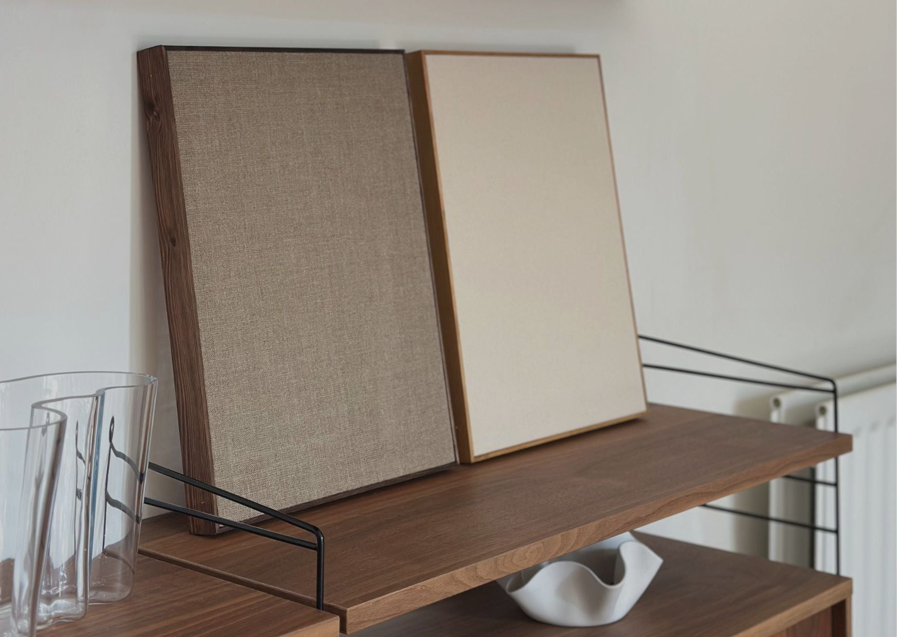 Two framed canvases in handcrafted wooden frames with natural cotton and linen, from Plan’s Blank Canvas Kits displayed on a wooden shelf. DIY art kits for adults offering a minimalist foundation for painting or creative projects.